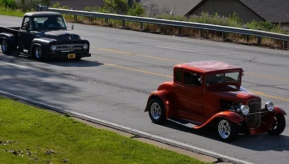 A red 1930s hot rod and a black Ford pickup cruising down the road