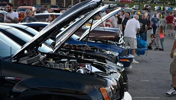 Rows of show cars with their hoods up and crowds walking between them